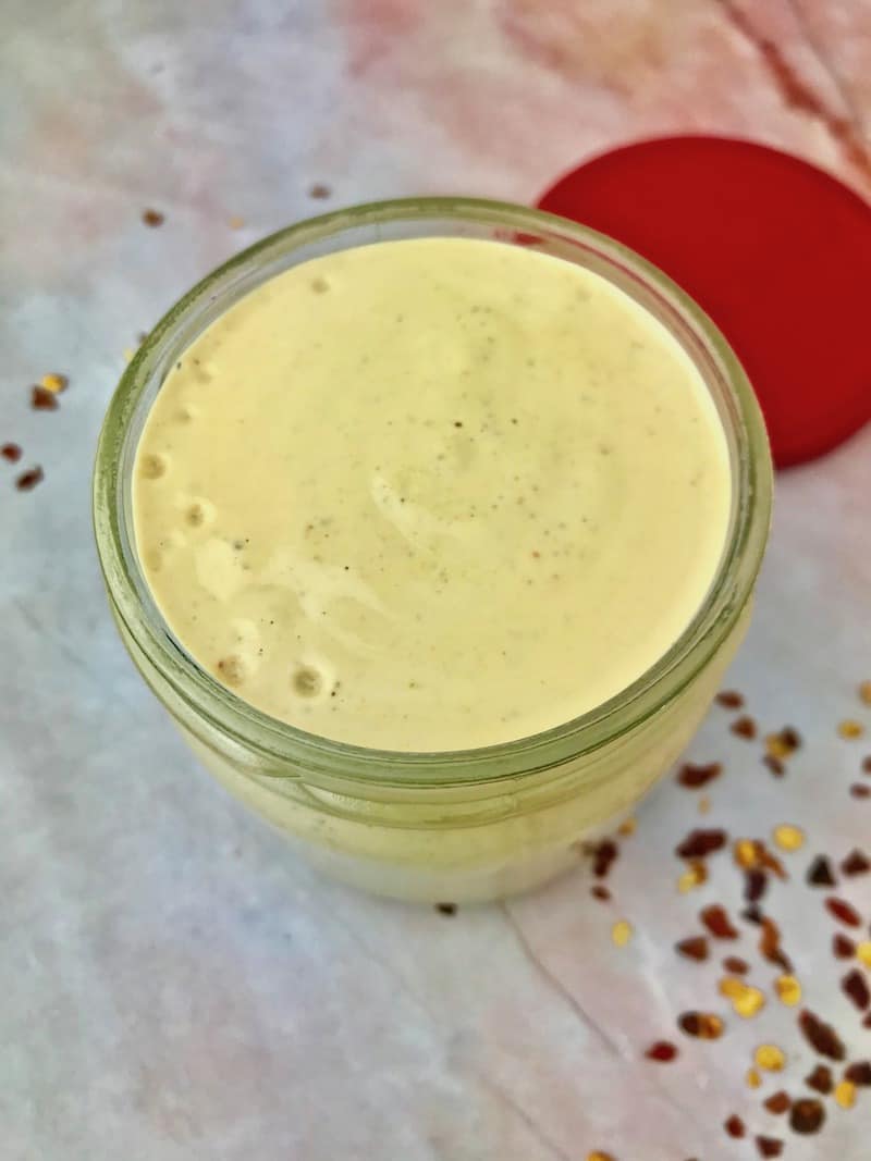 A jar of spicy cashew dressing next to crushed red pepper flakes.
