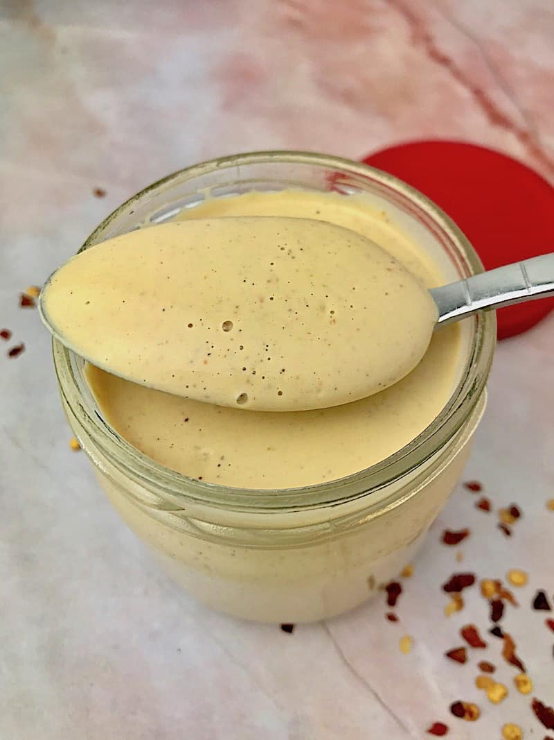 A jar of cashew dressing with a spoonful on top, next to crushed red pepper.