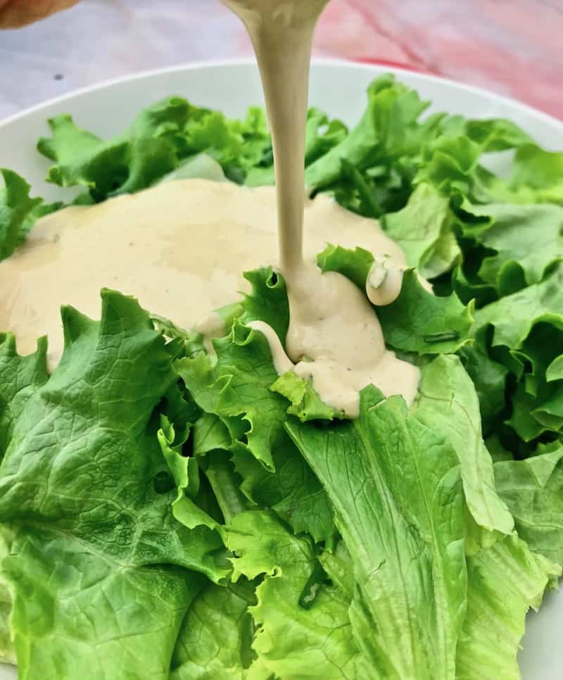 Dressing being poured onto a green salad.