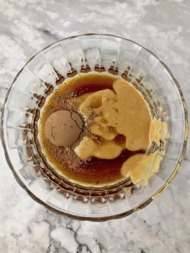 Peanut butter, cacao powder, and maple syrup in a small clear bowl.