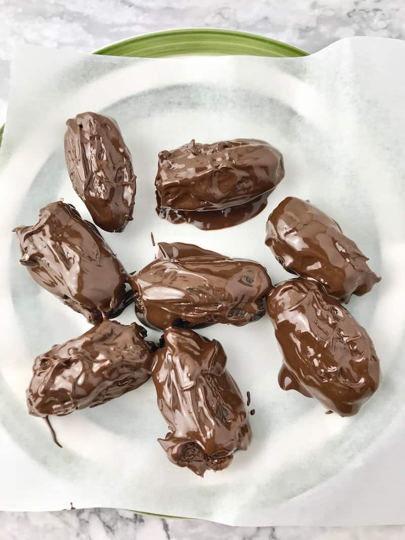 Dates dipped in melted chocolate, sitting on a parchment lined plate.