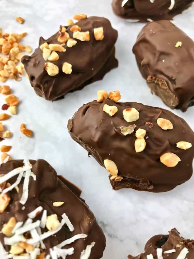 Chocolate covered dates with chopped peanuts and coconut on top of them.