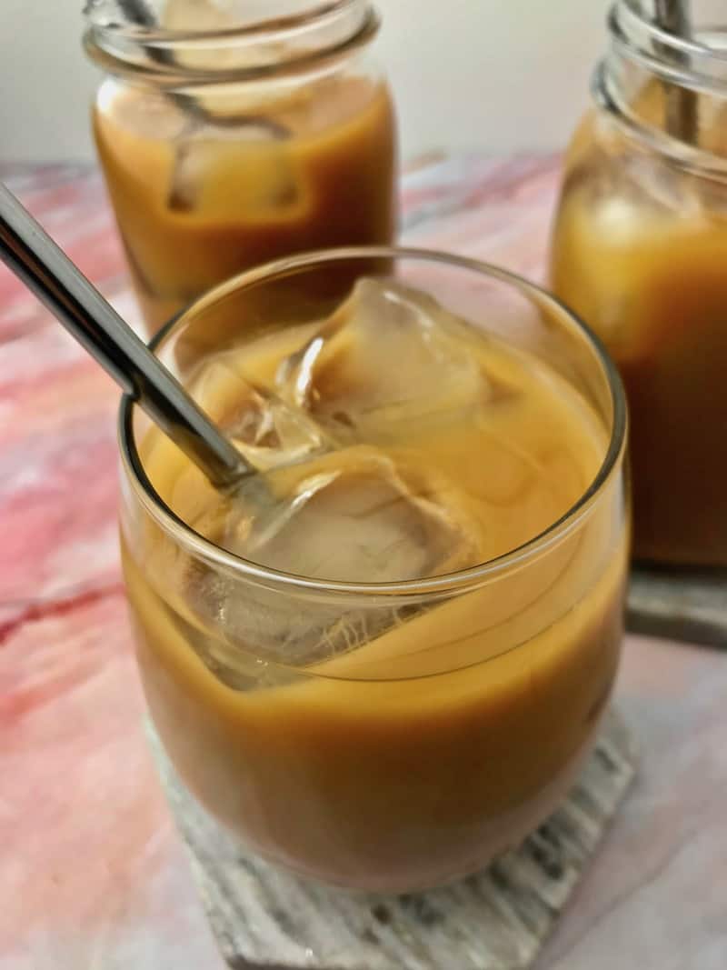 A glass of iced coffee, with two more iced coffees in the background.