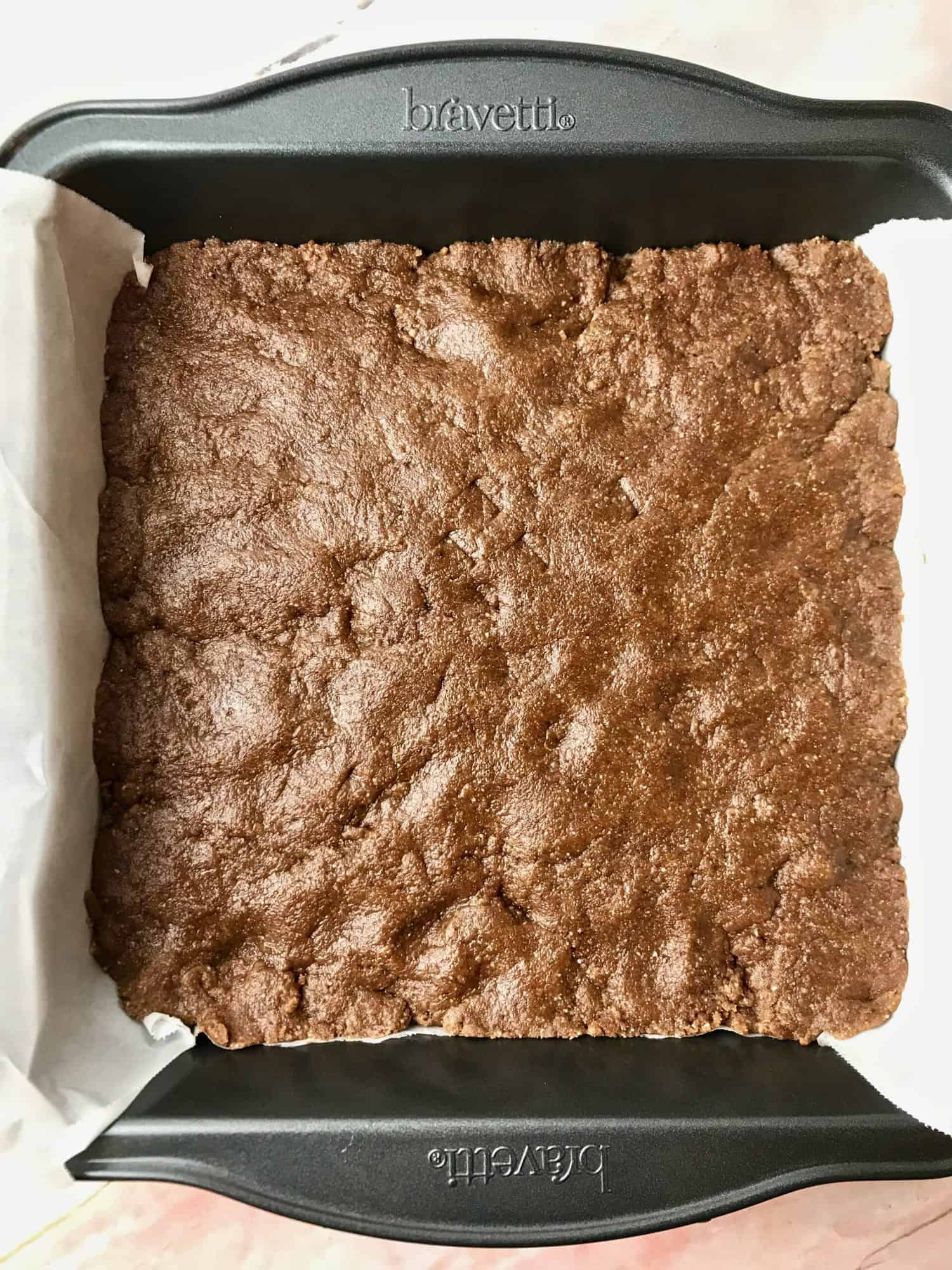 Chocolate almond bar mix pressed into a square pan.