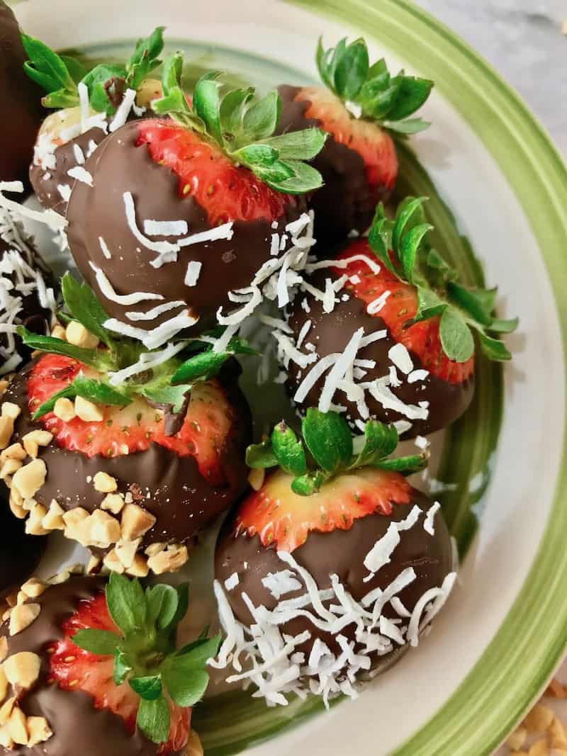 A plate of chocolate dipped strawberries with coconut flakes and chopped peanuts.