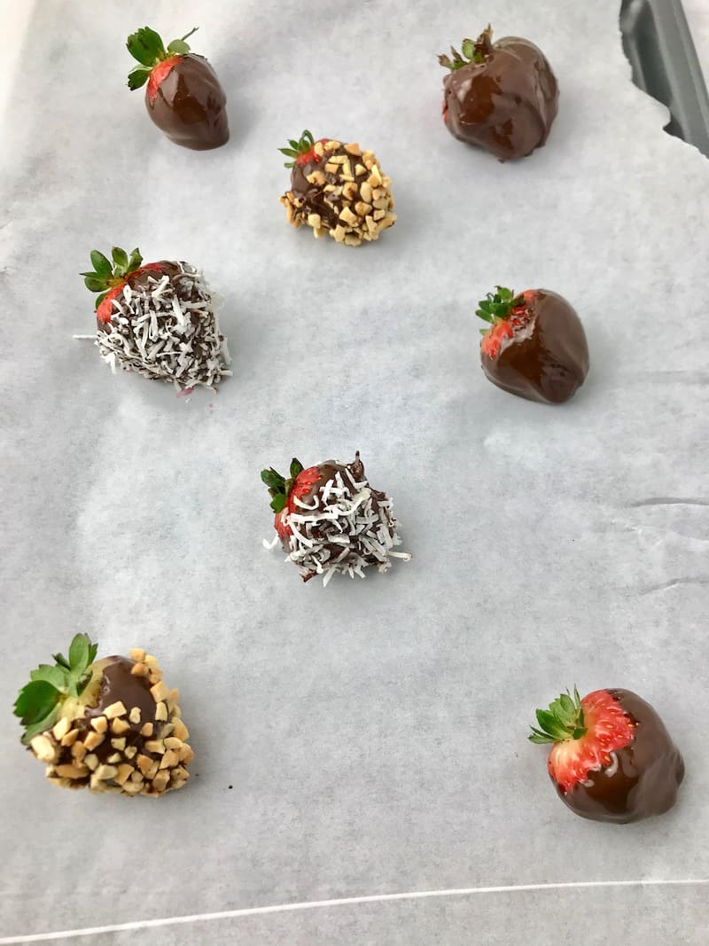 Chocolate dipped strawberries with toppings on parchment paper.