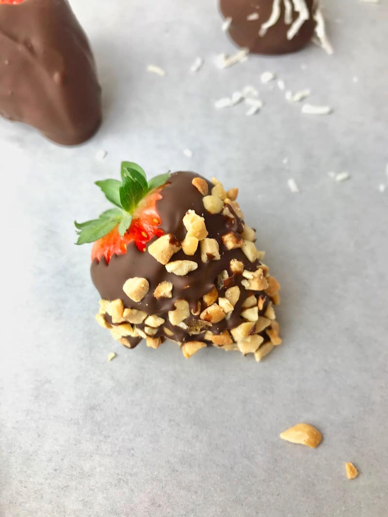 A chocolate covered strawberry with chopped peanuts on it.