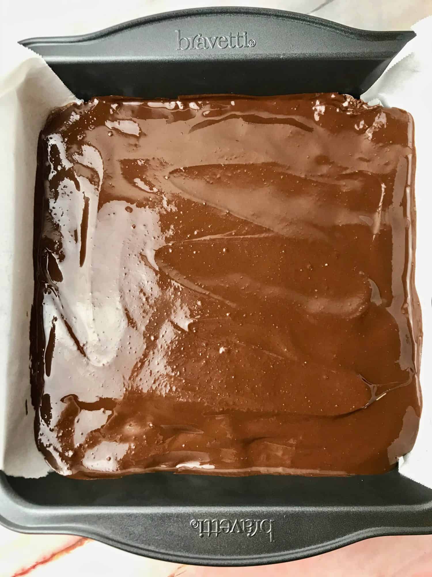 Melted chocolate spread over dough in a square pan.