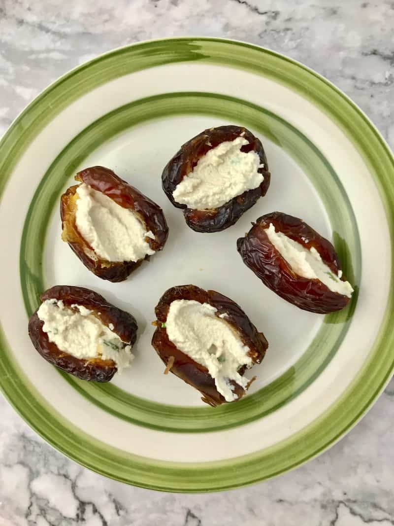 Medjool dates stuffed with vegan cream cheese, on a green and white plate.