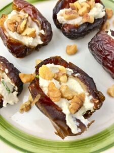 Dates with cream cheese and walnut pieces on a green and white plate.