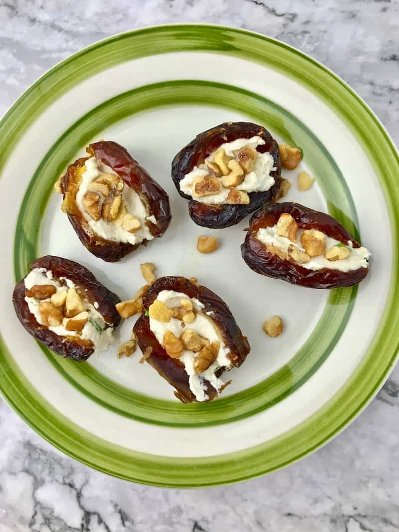 Medjool dates stuffed with vegan cream cheese and chopped walnuts on a plate.