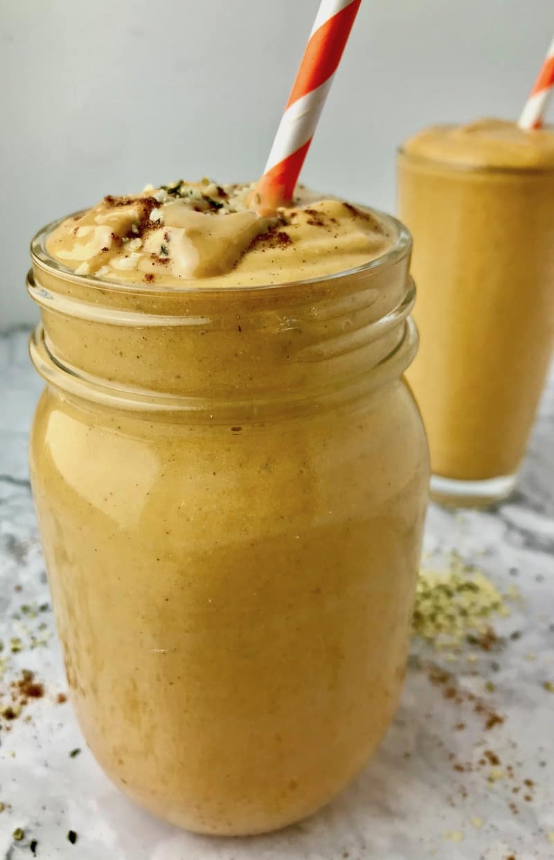 An orange smoothie in a mason jar with a straw.