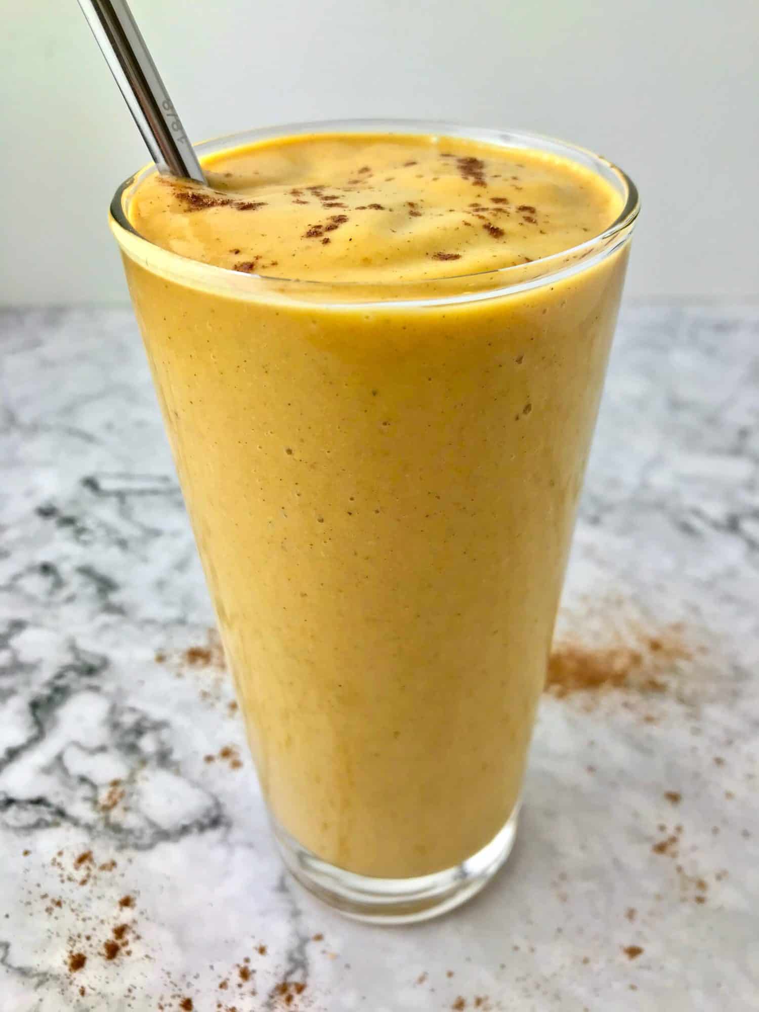 A sweet potato smoothie in a glass with a metal straw.