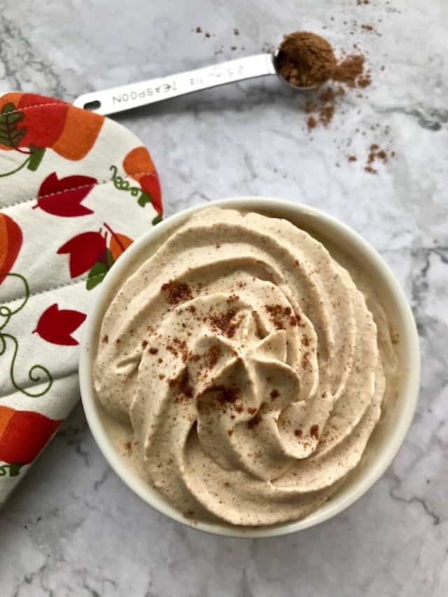 A bowl of whipped cream topped with pumpkin pie spice, next to an oven mitt.