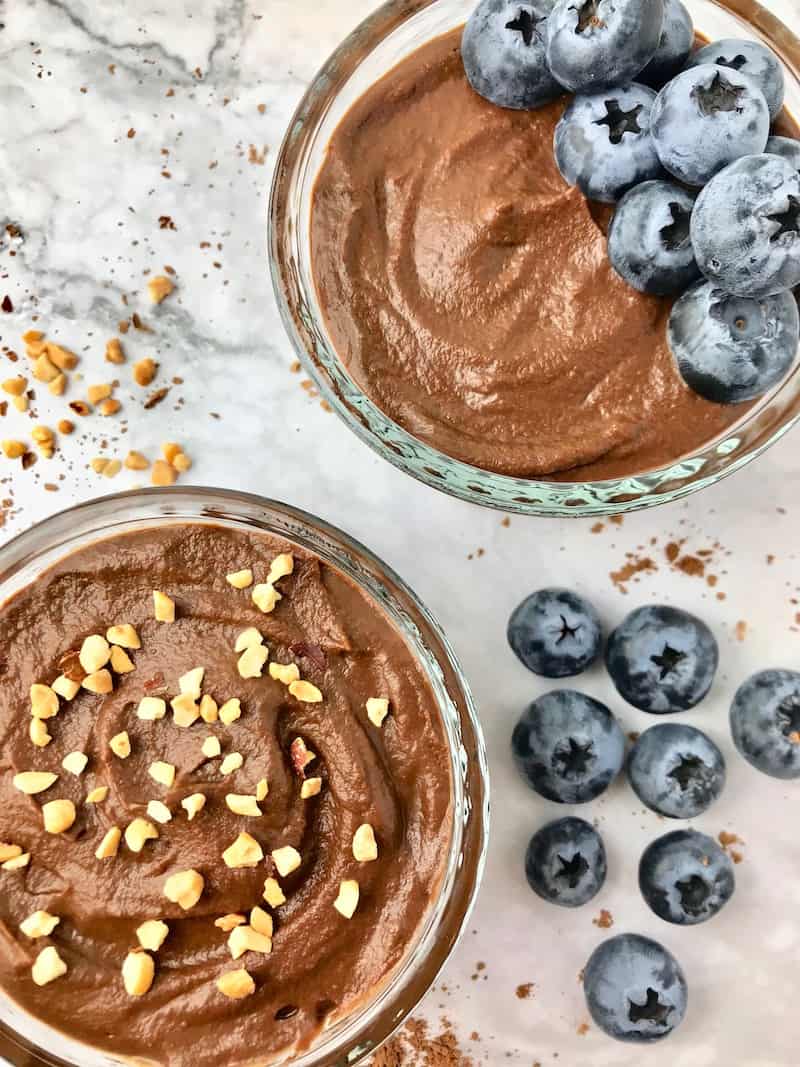 Two bowls of chocolate sweet potato pudding, one topped with peanuts and the other with blueberries.