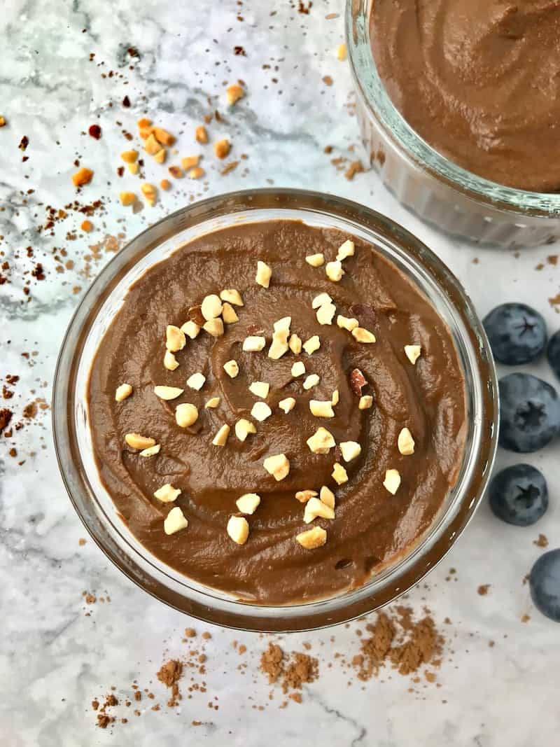 A bowl of chocolate pudding topped with chopped peanuts.