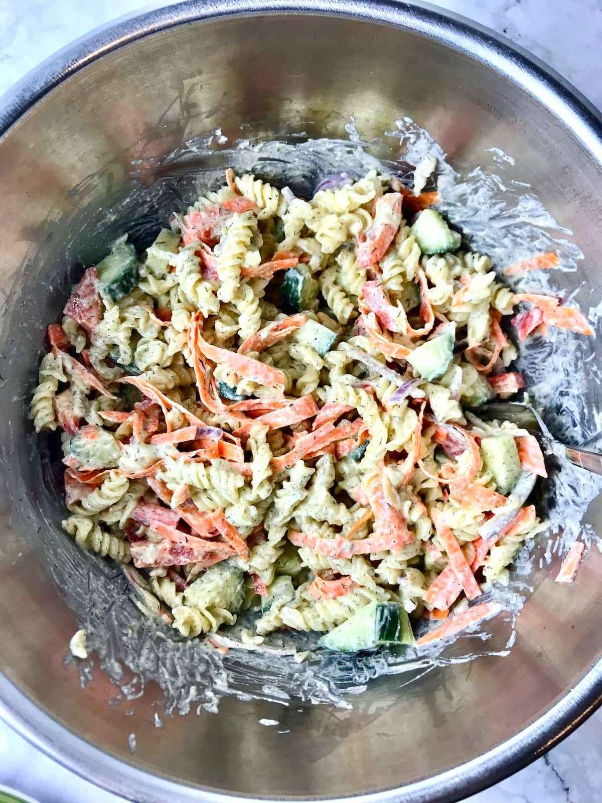 A bowl of pasta and veggies mixed with hummus dressing.