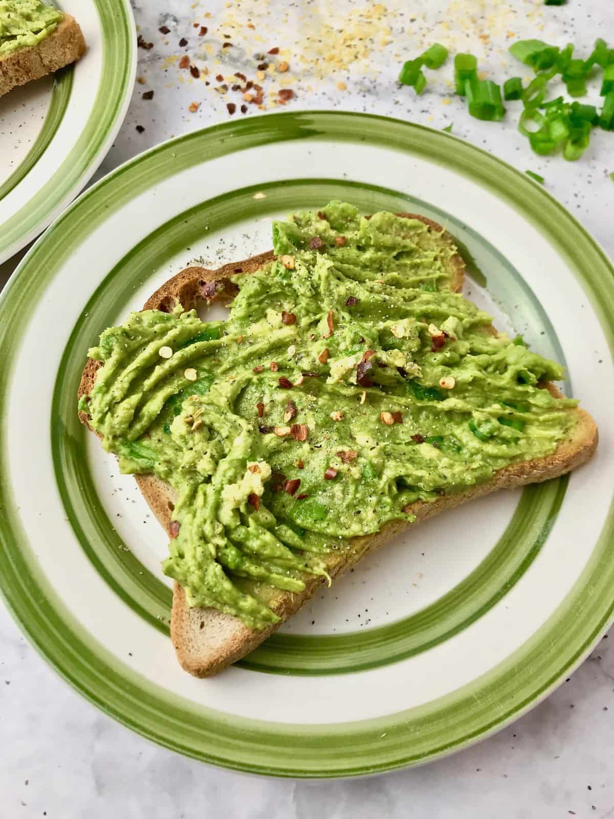 A piece of avocado toast on a plate, topped with red pepper flakes.