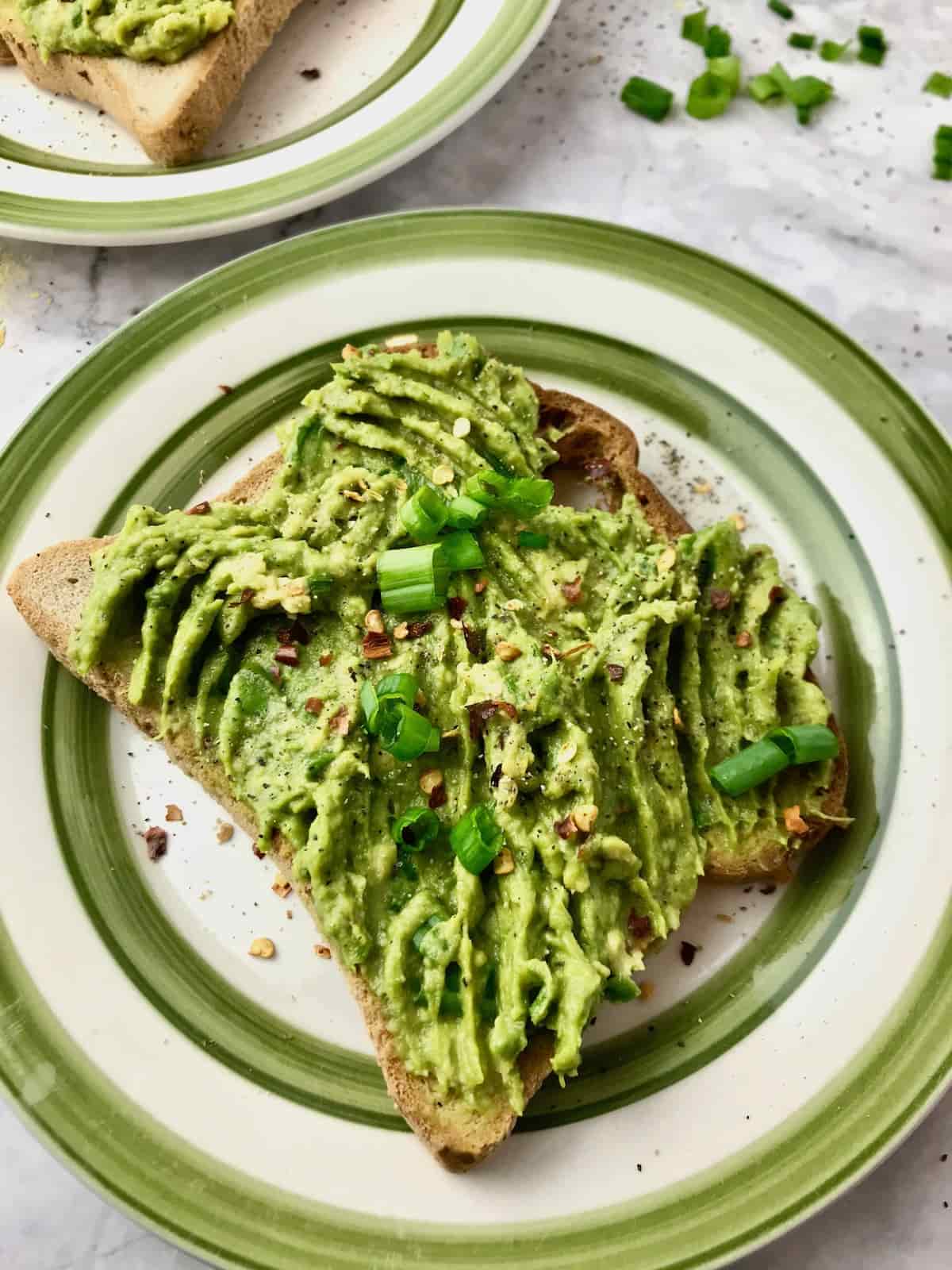 Avocado toast on a plate with green onions and red pepper flakes on top.