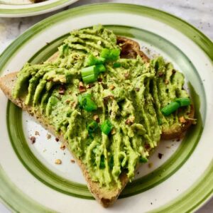 A piece of avocado toast topped with chopped green onion.