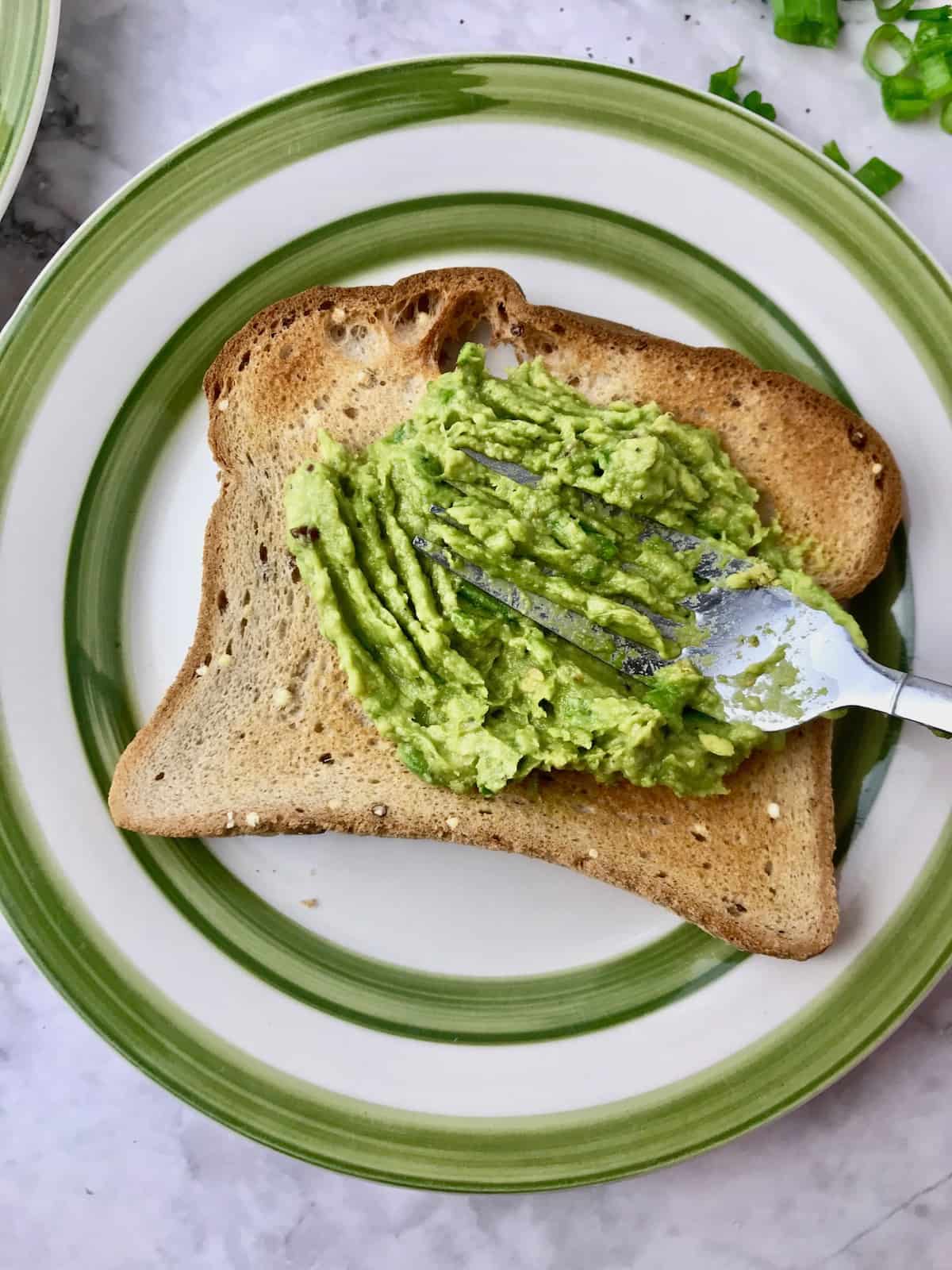 Avocado mix being spread on a piece of toast with a fork.