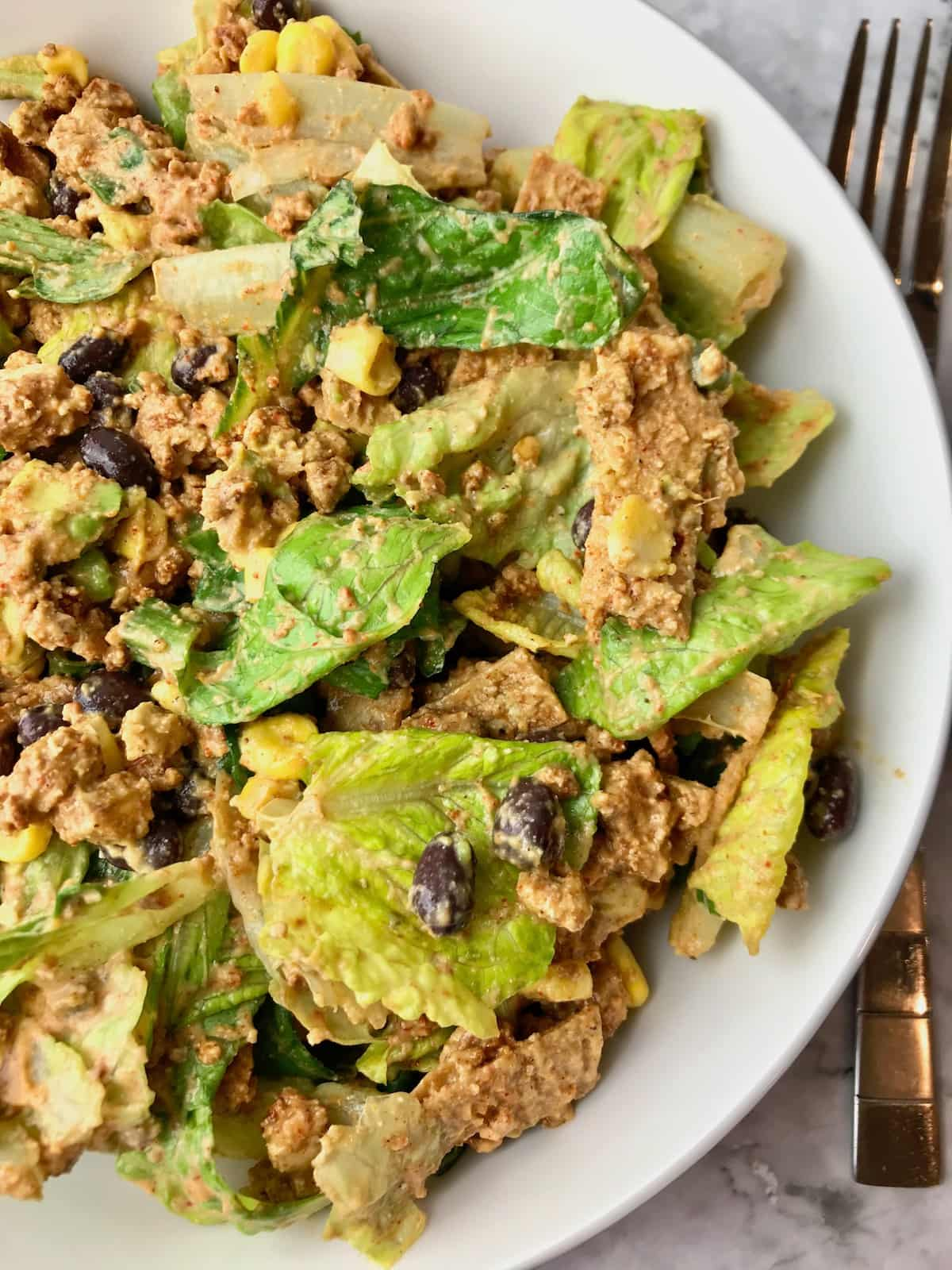 Half of a bowl of taco salad next to a fork.