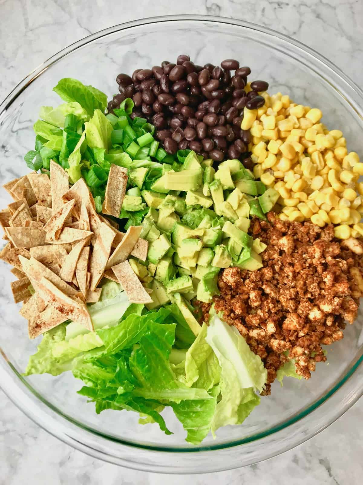 Black beans, corn, tofu, lettuce, tortilla strips, avocado, and lettuce in a bowl.