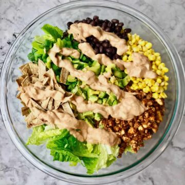 A bowl or taco salad ingredients topped with a beige salsa dressing.