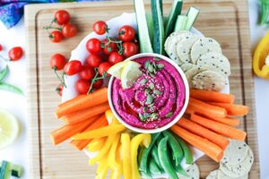 Beet hummus surrounded by chopped raw vegetables and crackers.