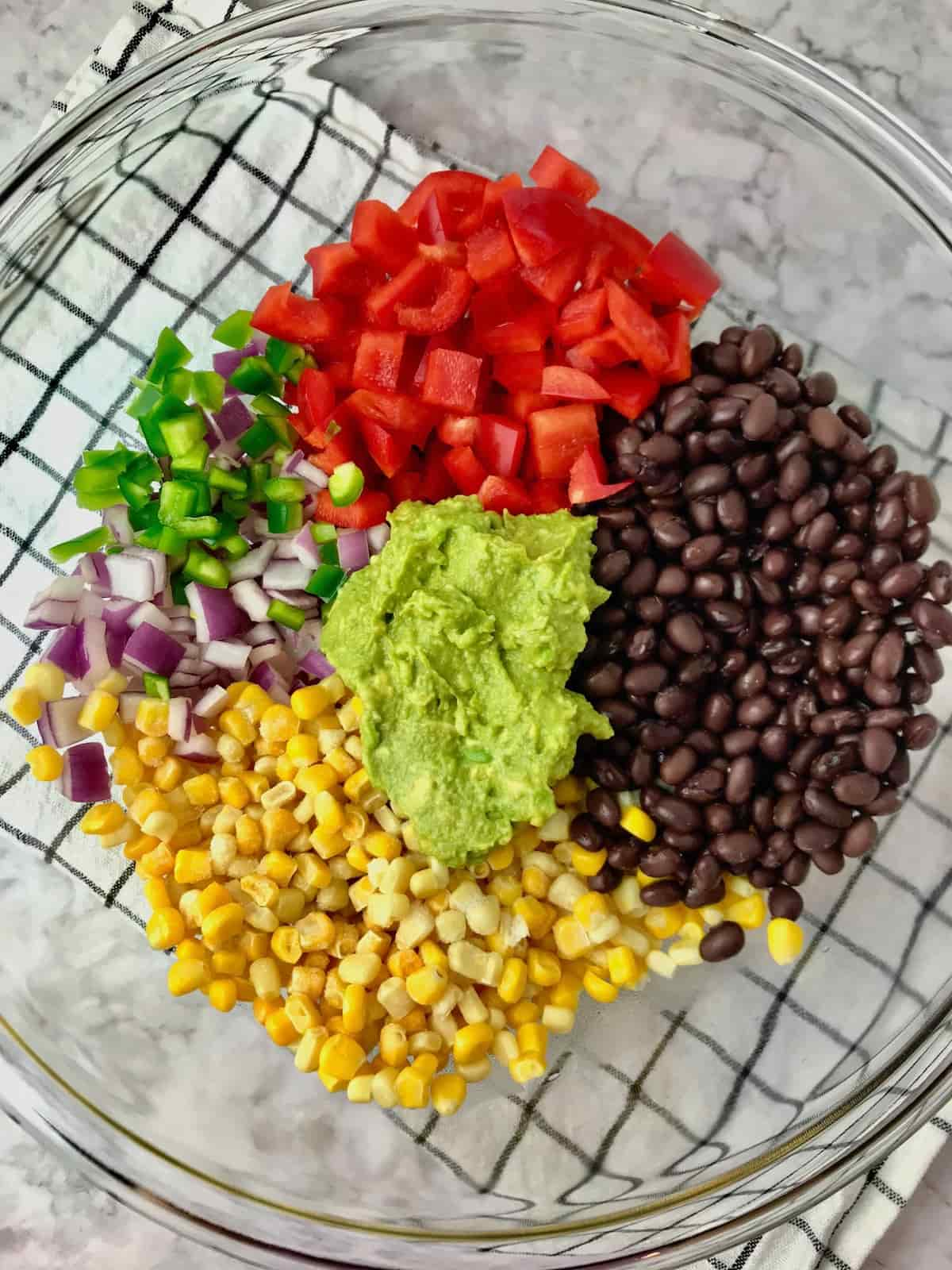 A bowl with red pepper, red onion, corn, black beans, jalapeno pepper and avocado.