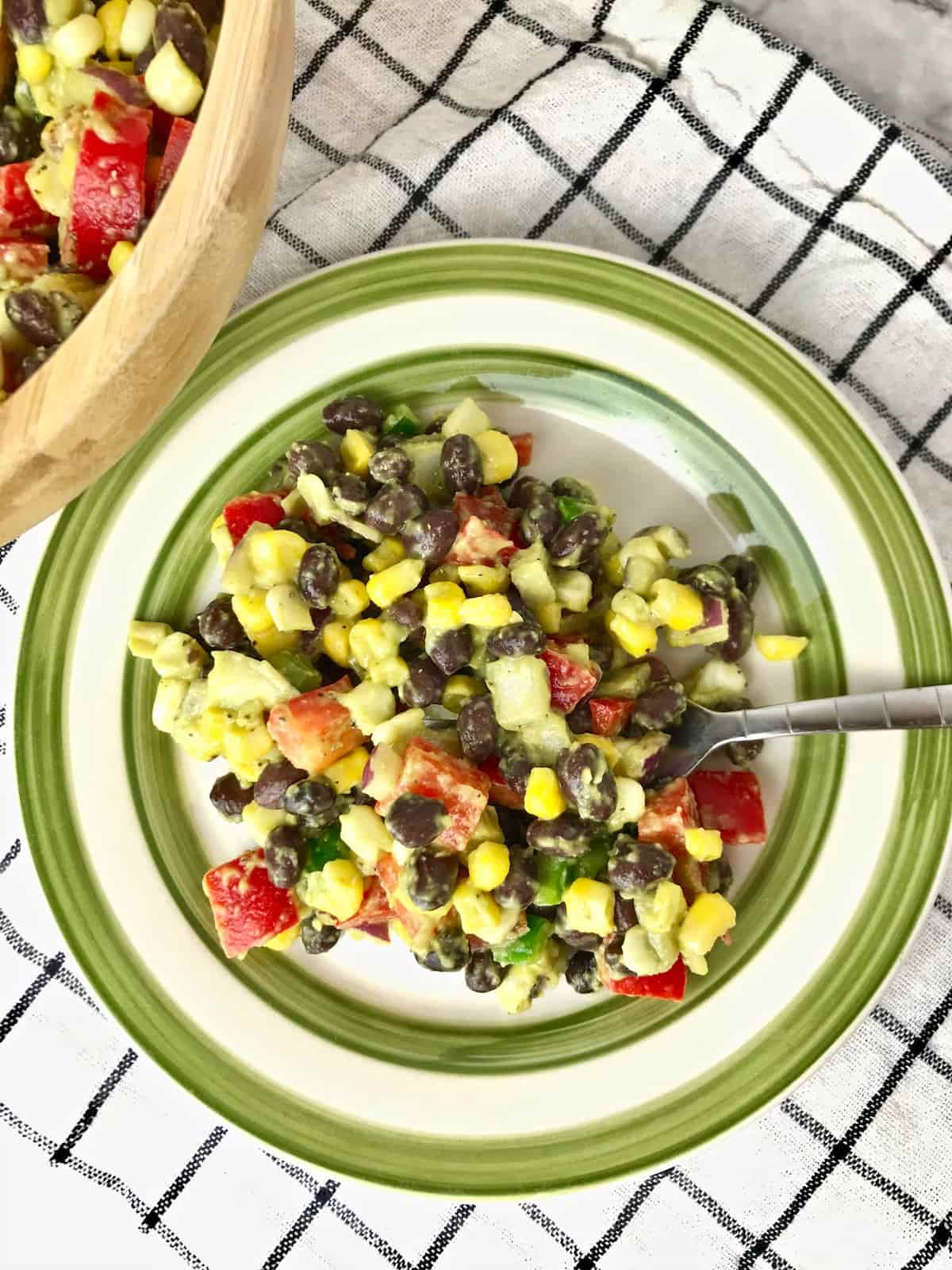 A green and white plate with corn and black bean salad on it.