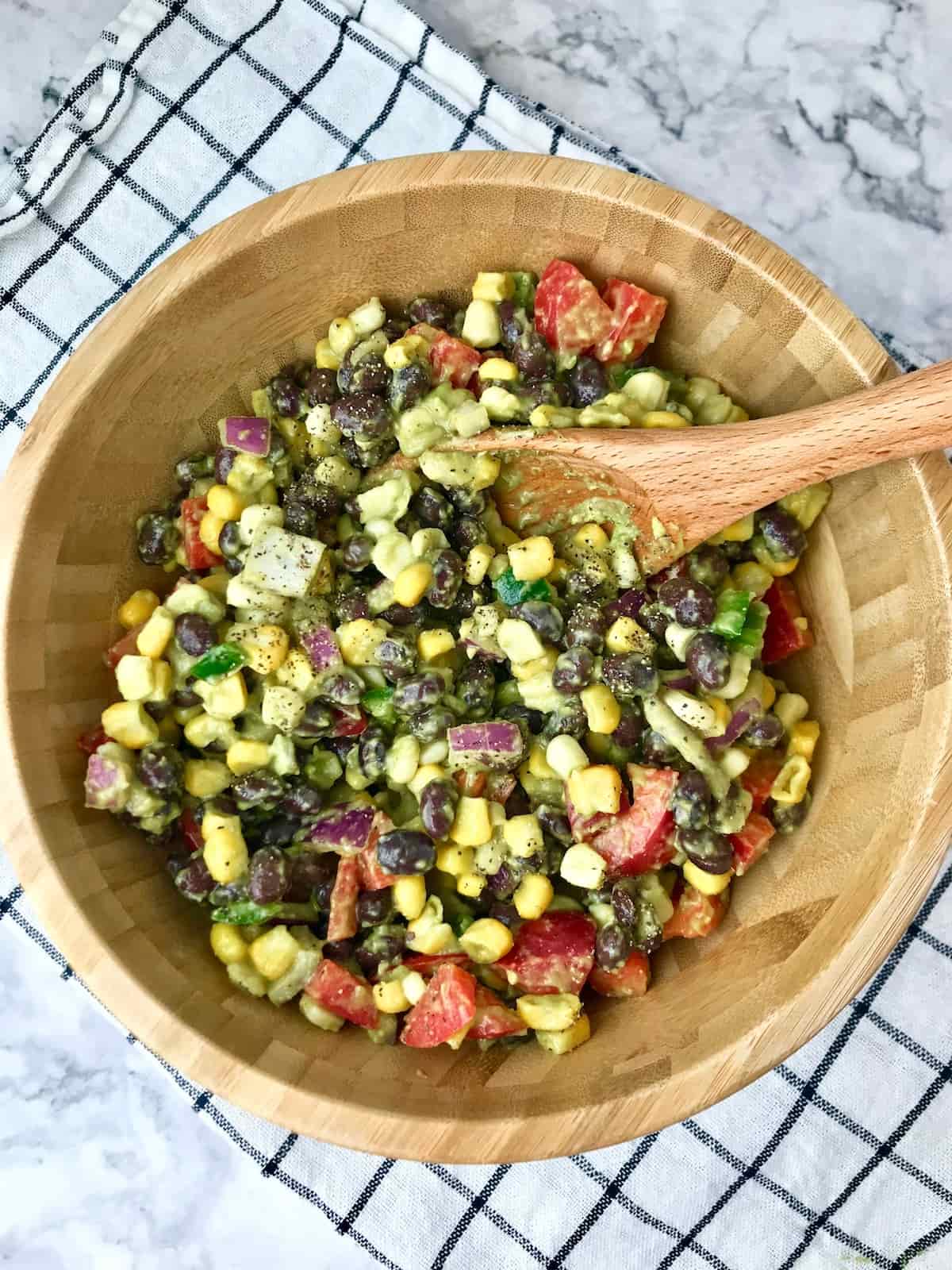 A bowl of black bean and corn salad on a black and white dish towel.