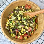 A bowl of black bean and corn salad with a wooden spoon in it.