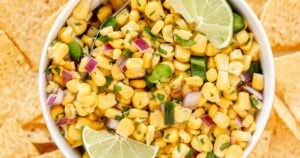 Corn salsa in a bowl with lime wedges, surrounded by chips.