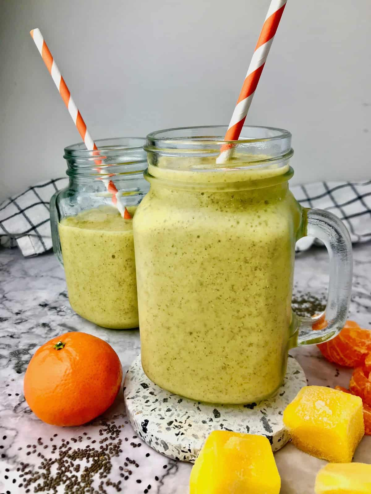 Two glasses of orange mango smoothie on a table next to oranges and mango chunks.