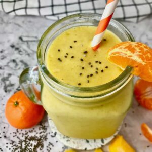 A smoothie in a mason jar with an orange slice on the rim and chia seeds sprinkled on top.