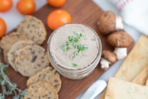 Mushroom pate in a container next to some crackers and mushrooms.