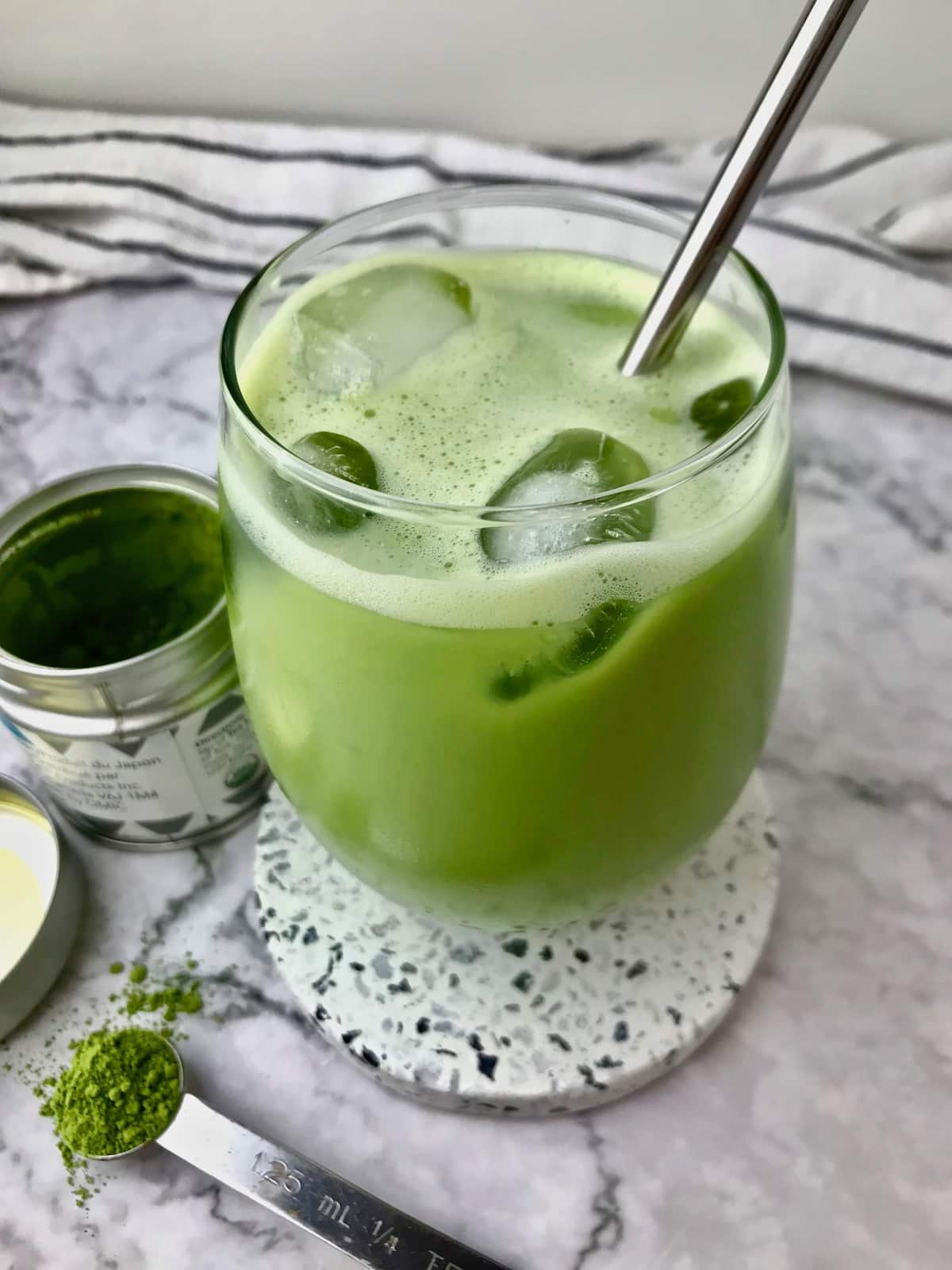 A green iced matcha latte next to some matcha powder.