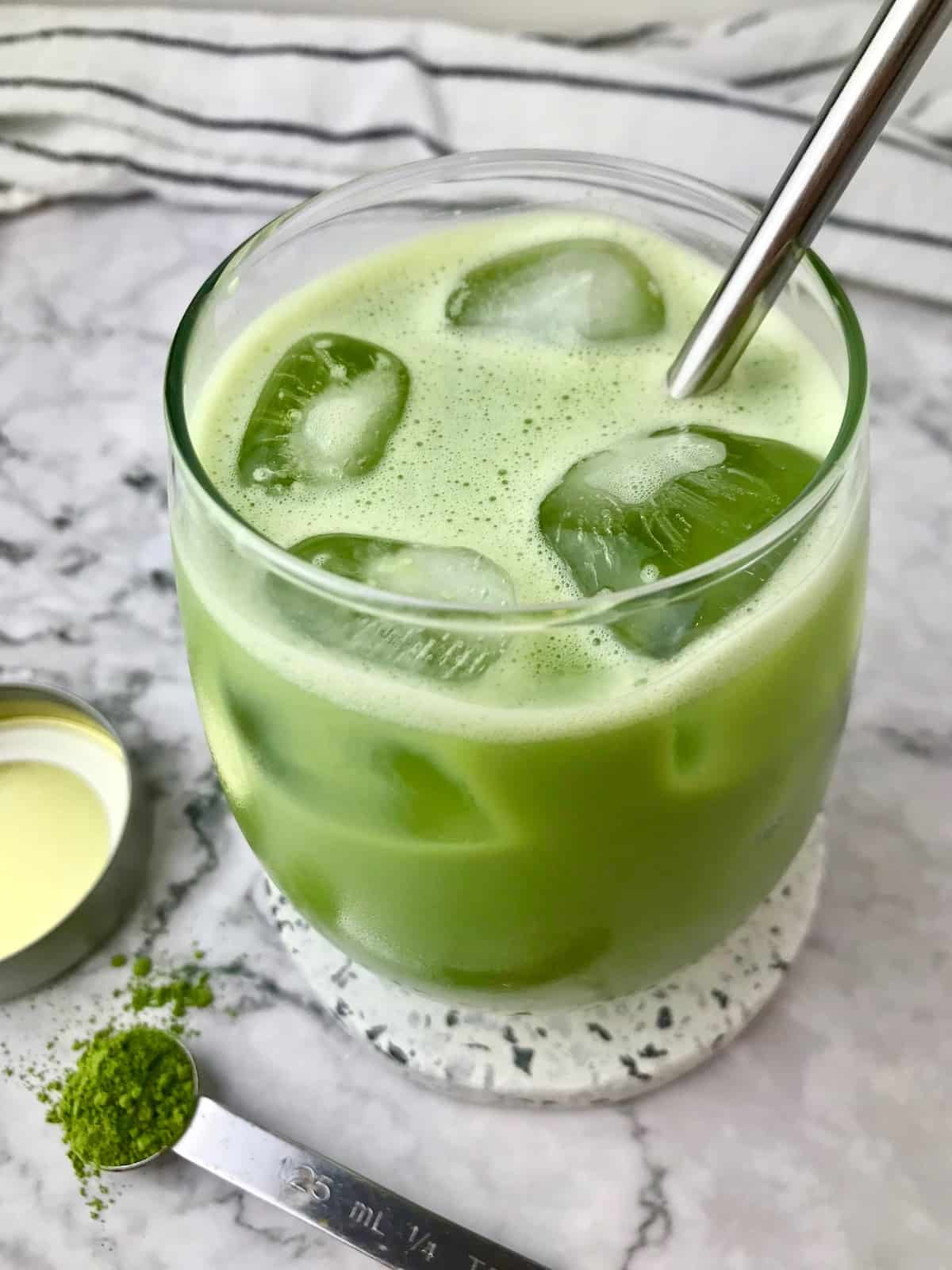 A green matcha latte with ice cubes and a metal straw in it.