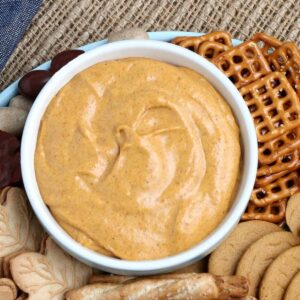 Vegan pumpkin dip in a small bowl surrounded by cookies and pretzels.