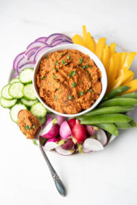 An orange romesco dip surrounded by fresh raw vegetables.