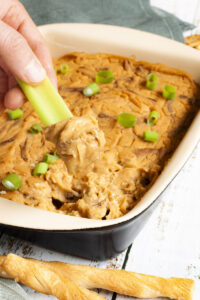 Vegan buffalo chicken dip in a dish with a celery stick being dipped into it.