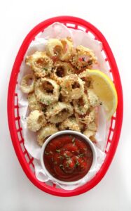 Vegan calamari in a container next to a lemon wedge and a bowl of ketchup.