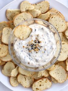 Everything bagel yogurt dip in a bowl surrounded by toasted bagel pieces.