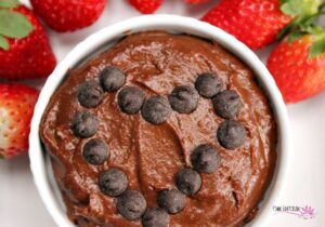 Brownie hummus topped with chocolate chips next to some strawberries.
