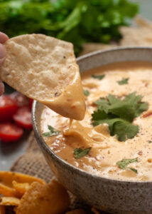 Vegan queso dip with a tortilla chip dipped into it.