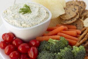 Vegan dill dip next to chips, crackers, and raw vegetables.