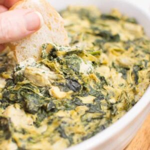 Vegan spinach artichoke dip with a piece of bread dipped into it.