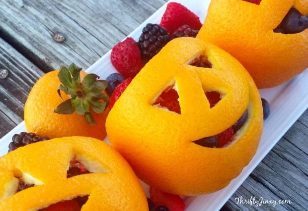 Orange peels cut like jack-o-lanterns with fruit inside of them.