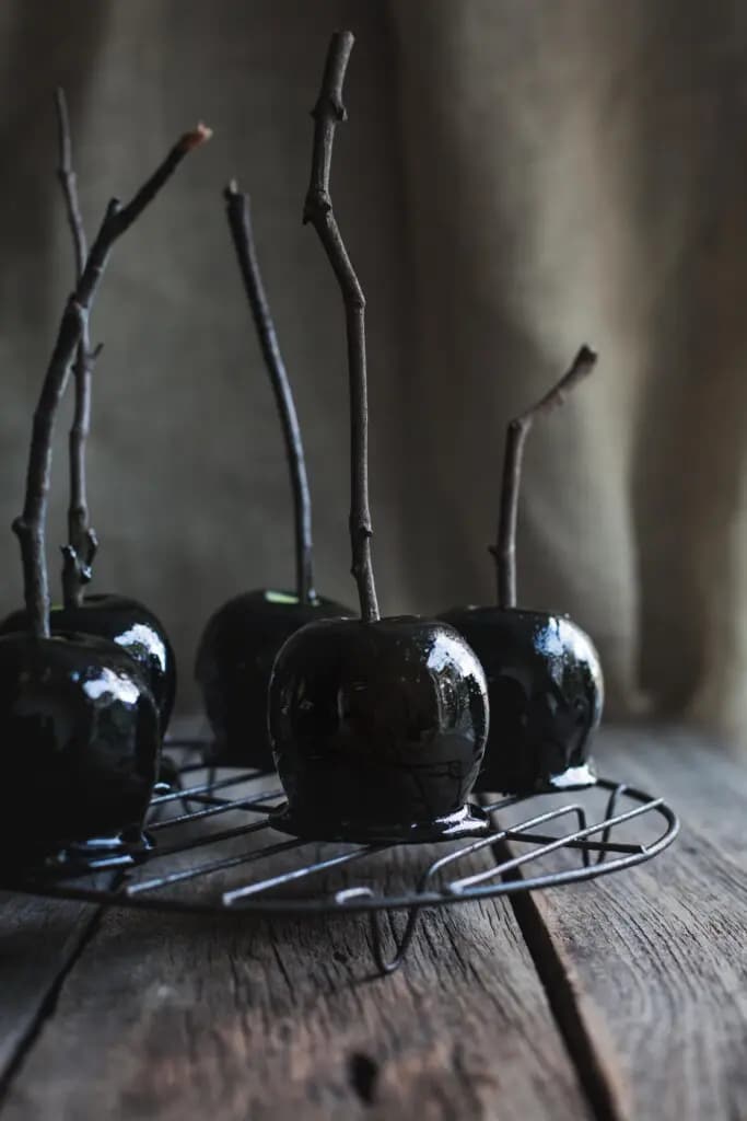 Apples covered in black toffee with sticks in them.